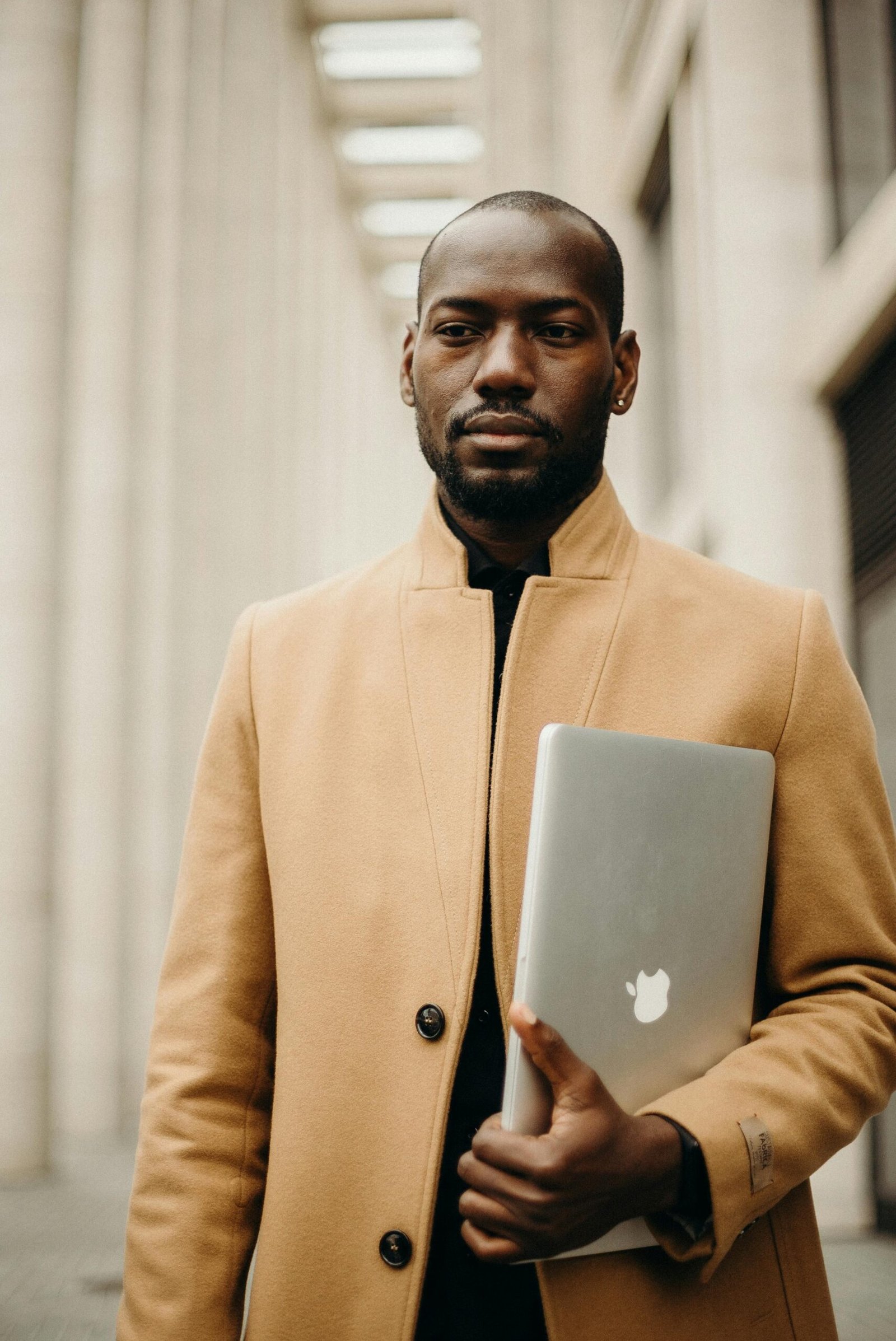 Stylish man holding a laptop, exuding professionalism in an urban environment.