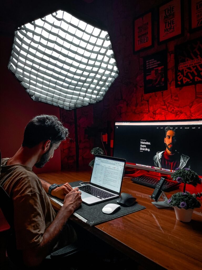 Asian man working at a laptop in a stylish red-lit room with modern equipment and lighting.