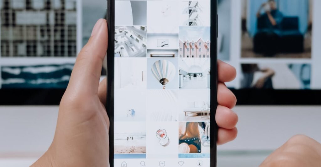 Person using smartphone to browse photos, office desktop setup.