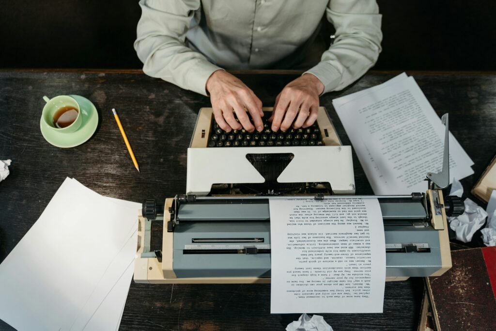 Hands typing on a vintage typewriter with papers and a coffee cup in view.